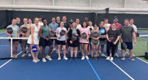 A group of people standing on a pickleball court holding pickleball rackets